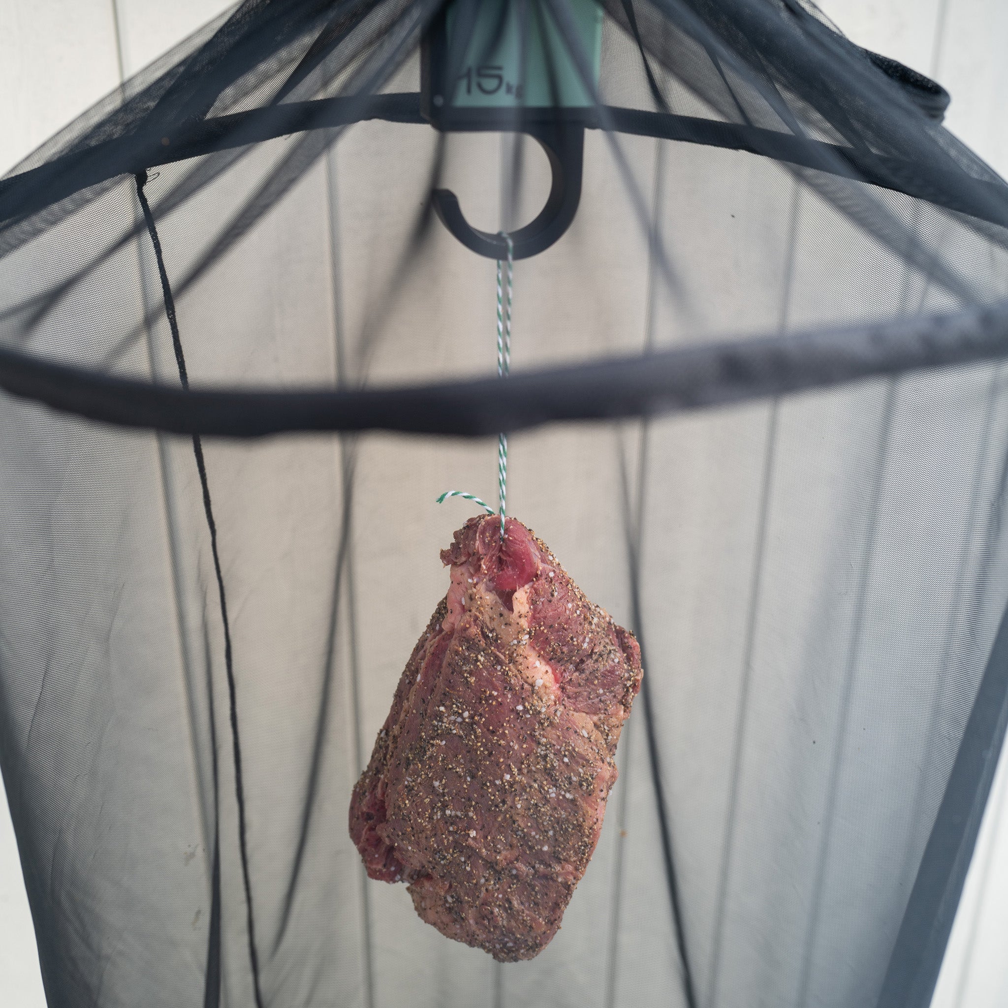 Marinated piece of meat hanging from a hook with a safety net to protect against flies