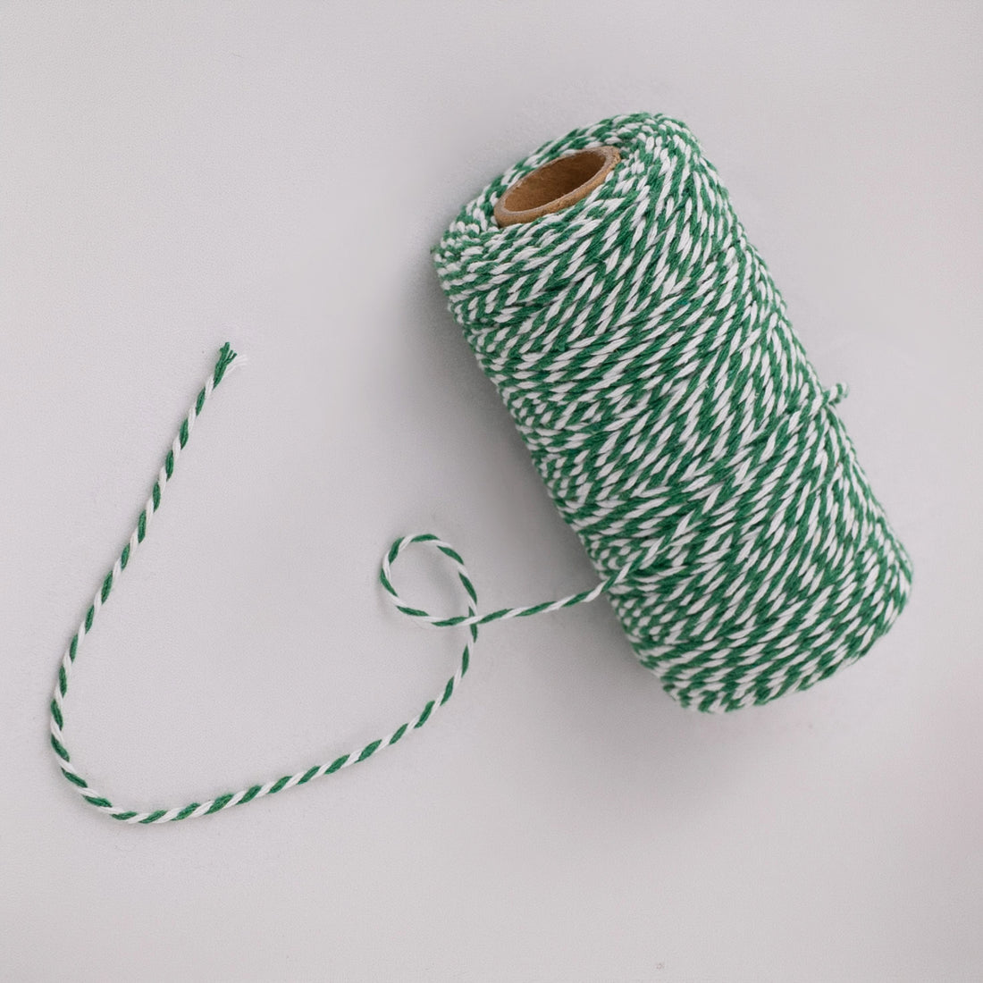 Roll of green and white striped butcher string, butcher twine, meat string, meat twine on a light gray background