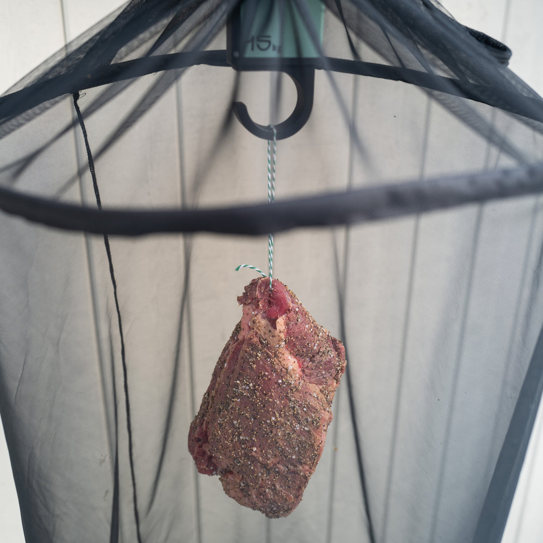 Marinated piece of meat hanging from a hook with a safety net to protect against flies