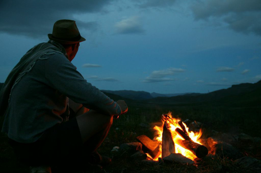 Person sitting by a campfire at night with mountains in the background with charcuterie snacks