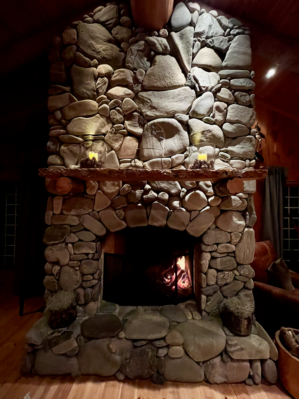 Stone fireplace with a fire burning inside, surrounded by wooden furniture.