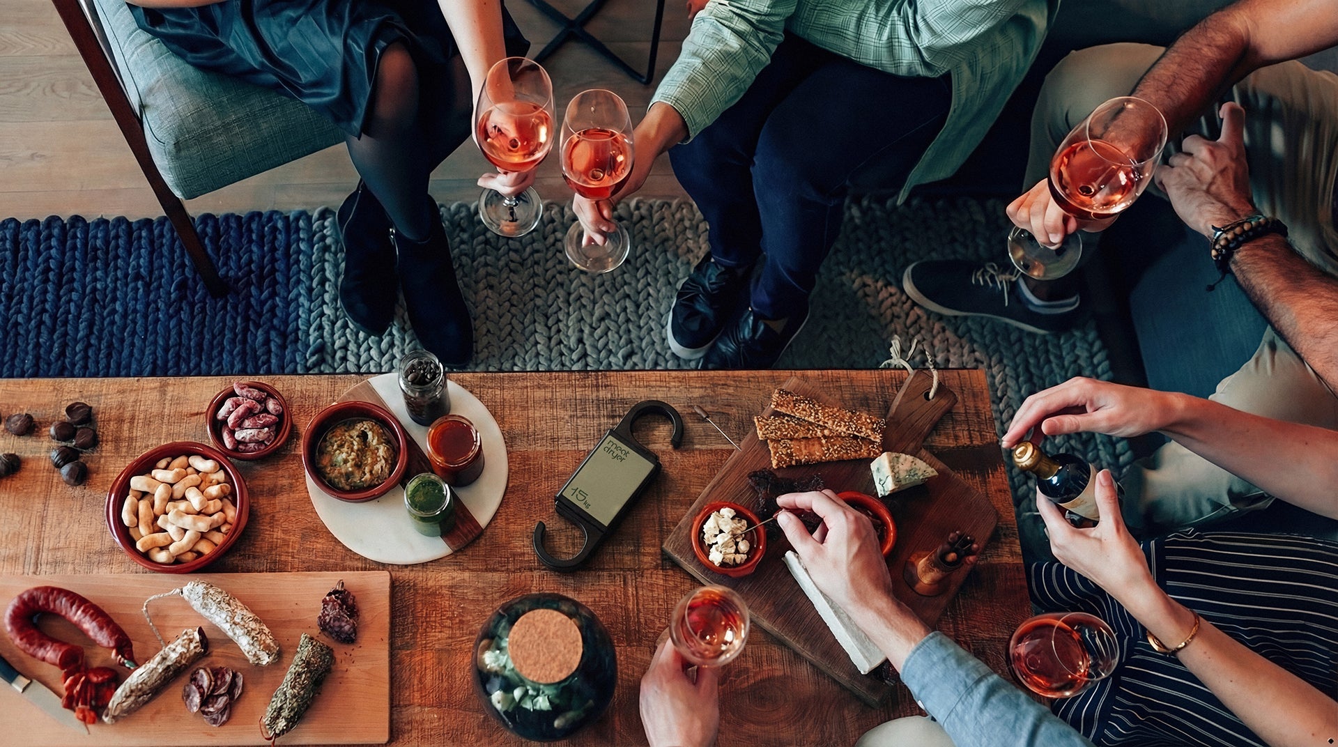 People sitting around a wooden table with food and drinks, toasting and enjoying salami, charcuterie.