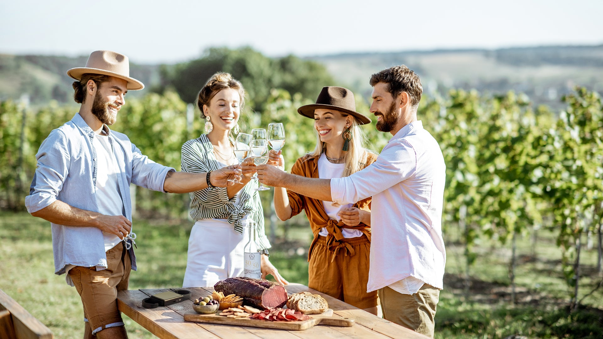 Four friends enjoying a picnic with wine and food in a vineyard, with cheese, coppa, speck or bresaola